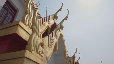 slow motion clip pointing up a popular thai buddhist temple while slowly walking around to show the roof and architecture on a very sunny and hot day