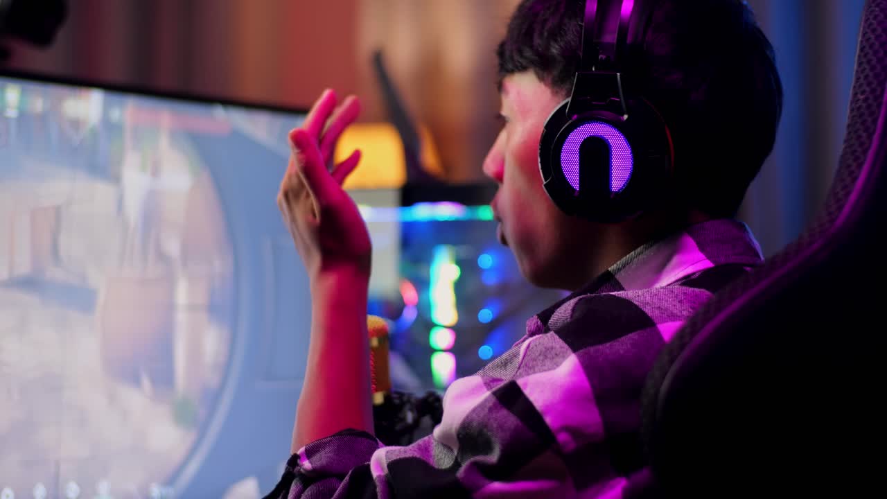 Close Up Back View Of Asian Boy Streamer Playing Game Over Network On Personal Computer. Challenge And Bully Competitor, Live Stream Video Game, Desk Illuminated By Rgb Led Strip Light
