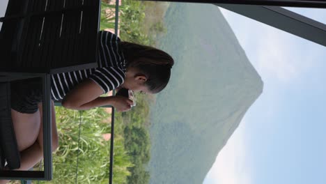 vertical shot of a girl drinking a cup of coffee in front of the arenal volcano in costa rica