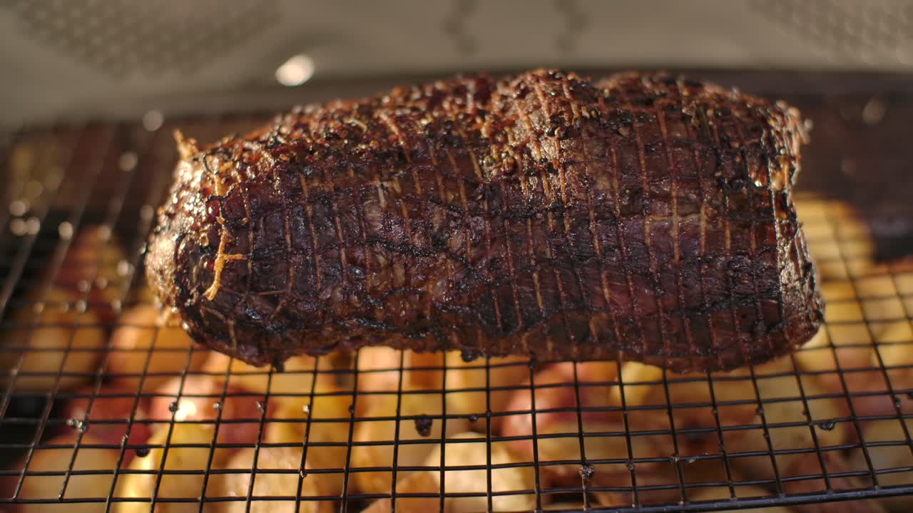 Close up of a seasoned beef roast sitting on a wire rack above roasted potatoes inside a hot oven