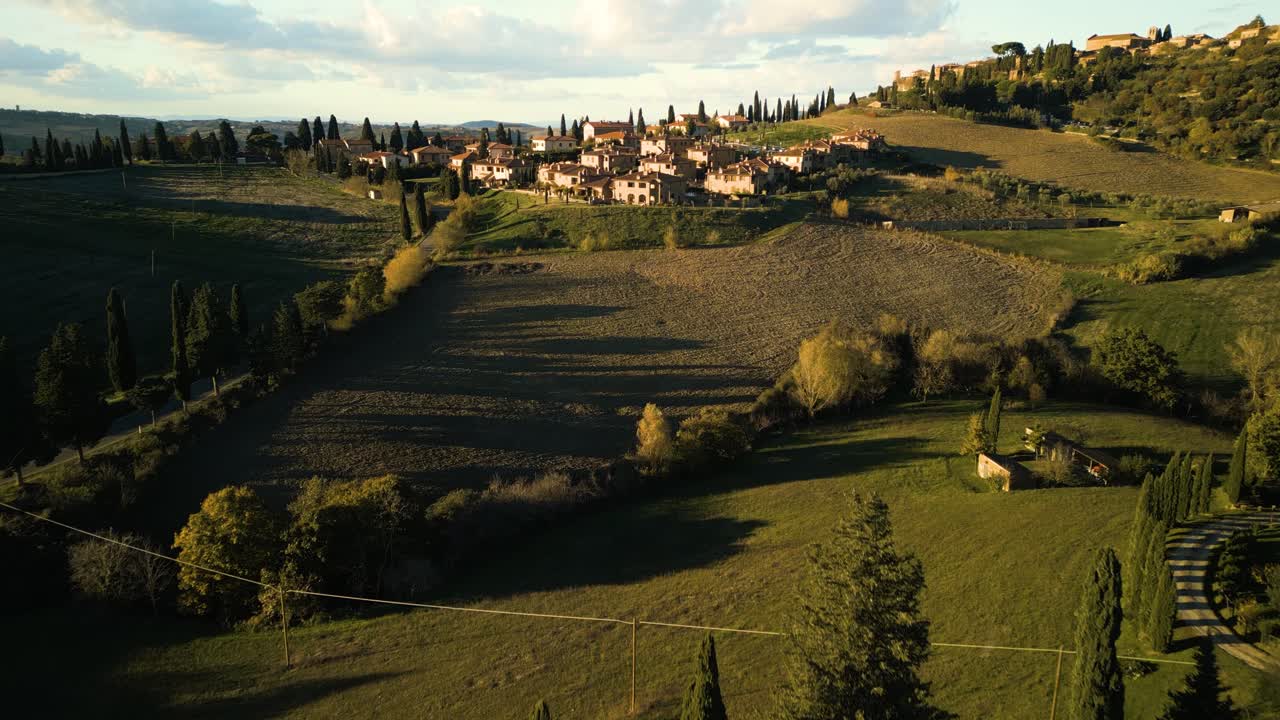 Golden hour light glows across rolling hills landscape of Val d'Orcia Tuscany with quaint village