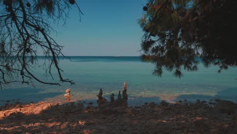 looking over the horizon at a scenic natural romantic calm water beach with small waves at the croatian mediterranean seaside with trees and hippie stone towers and clear blue water. outdoors tourism vacation sunset cinemagraph seamless video loop in 4k.