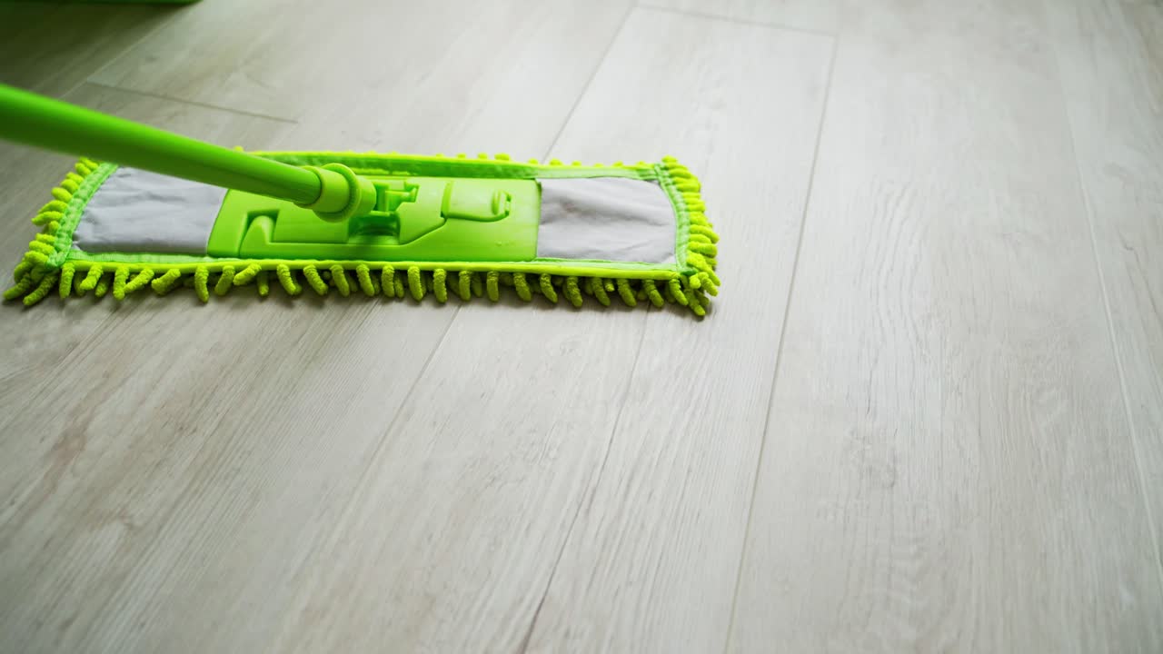 Modern mop on the wooden floor background. Cleaning the parquet floor by a green microfiber brush. Housekeeping routine.