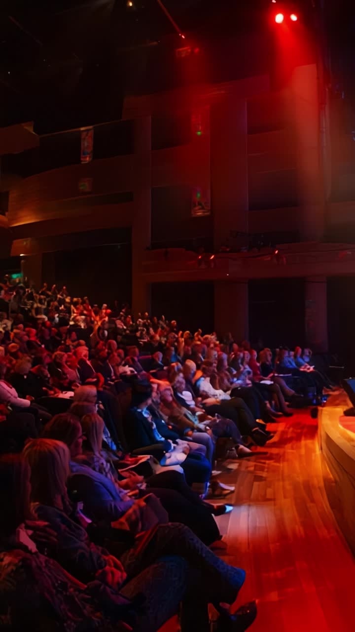 Pubblico coinvolto in un teatro con illuminazione dinamica che cattura l'energia e l'attesa durante un discorso o un evento di presentazione dal vivo