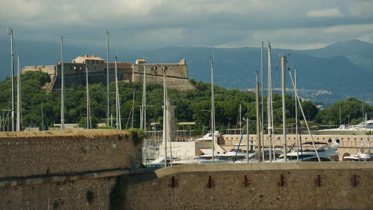 Vista de Port Vauban e Fort Carré, com mastros de veleiros, muralhas de pedra históricas e montanhas ao fundo, Antibes, França