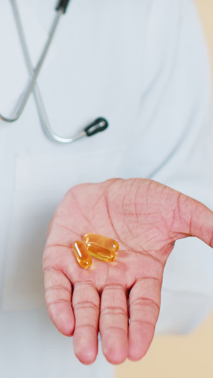 Medico mostra pillole/compresse di Omega 3 nel palmo della mano, raccomandando farmaci, vitamine, vaccinazioni e trattamenti