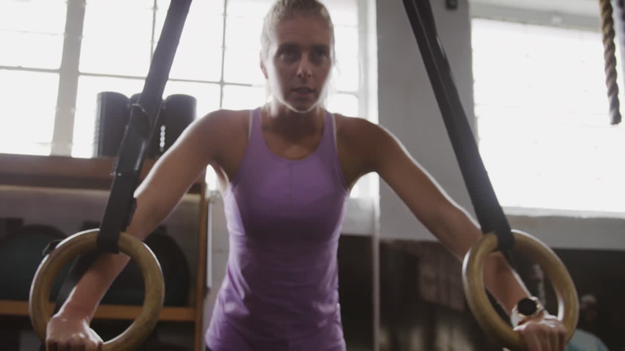 Vista frontale di una donna caucasica atletica che si tiene agli anelli da ginnastica