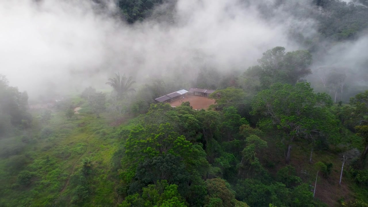 Filmato aereo con drone di nuvole che passano sopra una casa isolata in cima a una collina, circondata da foresta pluviale e palme nell'Amazzonia ecuadoriana in una mattina nebbiosa