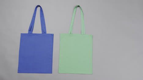 Close-up-of-blue-and-green-bags-on-grey-background,-with-copy-space,-slow-motion