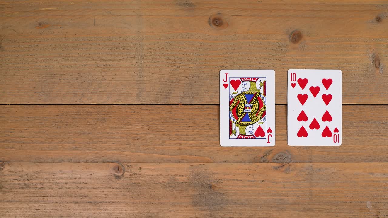 A person laying out a royal flush with hearts on a wooden table to educate the viewer on how to play poker