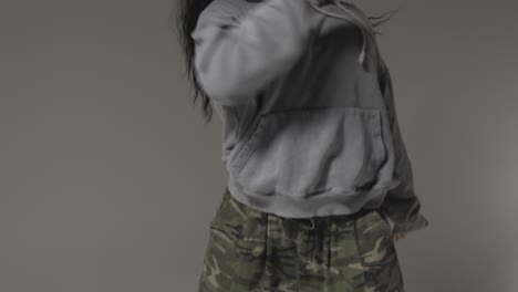 studio shot of young woman wearing hoodie dancing with low key lighting against grey background