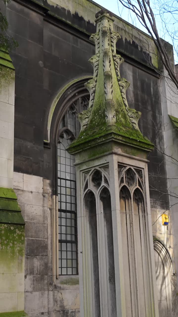 Complicate cornici di finestre in pietra e archi gotici in rovina del giardino della storica chiesa di St Dunstan in the East, che mostrano l'incrocio tra muratura antica e piante rampicanti.