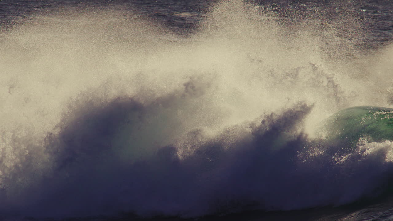 Barrel wave crashes fast in backlit light, intense white splash and frothy crest trail