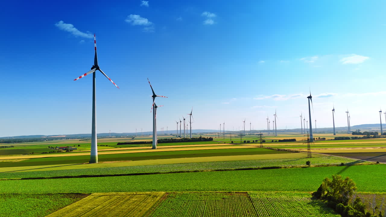 Rising over the green field on sunny day. Multiple windmills rotate producing clean energy.