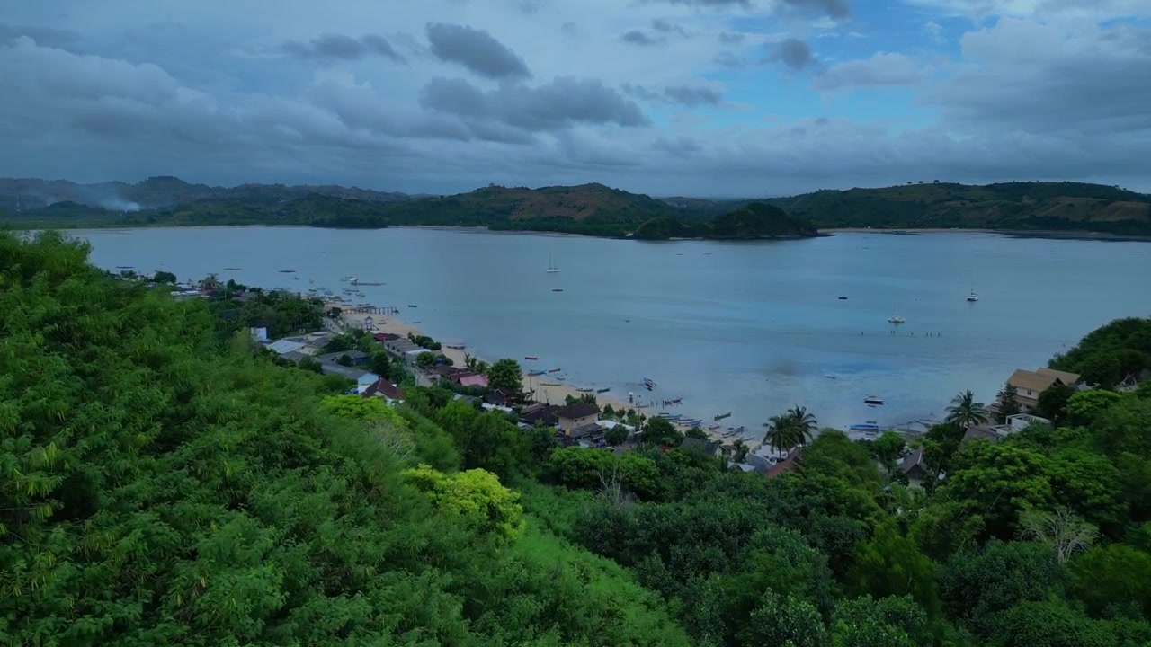 Scoprendo l'isola tropicale di Lombok con vaste colline coperte da una fitta vegetazione verde che incontrano le calme acque della baia sotto un cielo nuvoloso. Migliore vista aerea, sorvolo panoramico con drone.