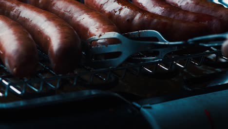 turning rotating fresh german sausages on electric bbq grill tongs green eco cooking global warming alternative bratwurst traditional bavarian cusine gloomy electrical beef pork minced meat