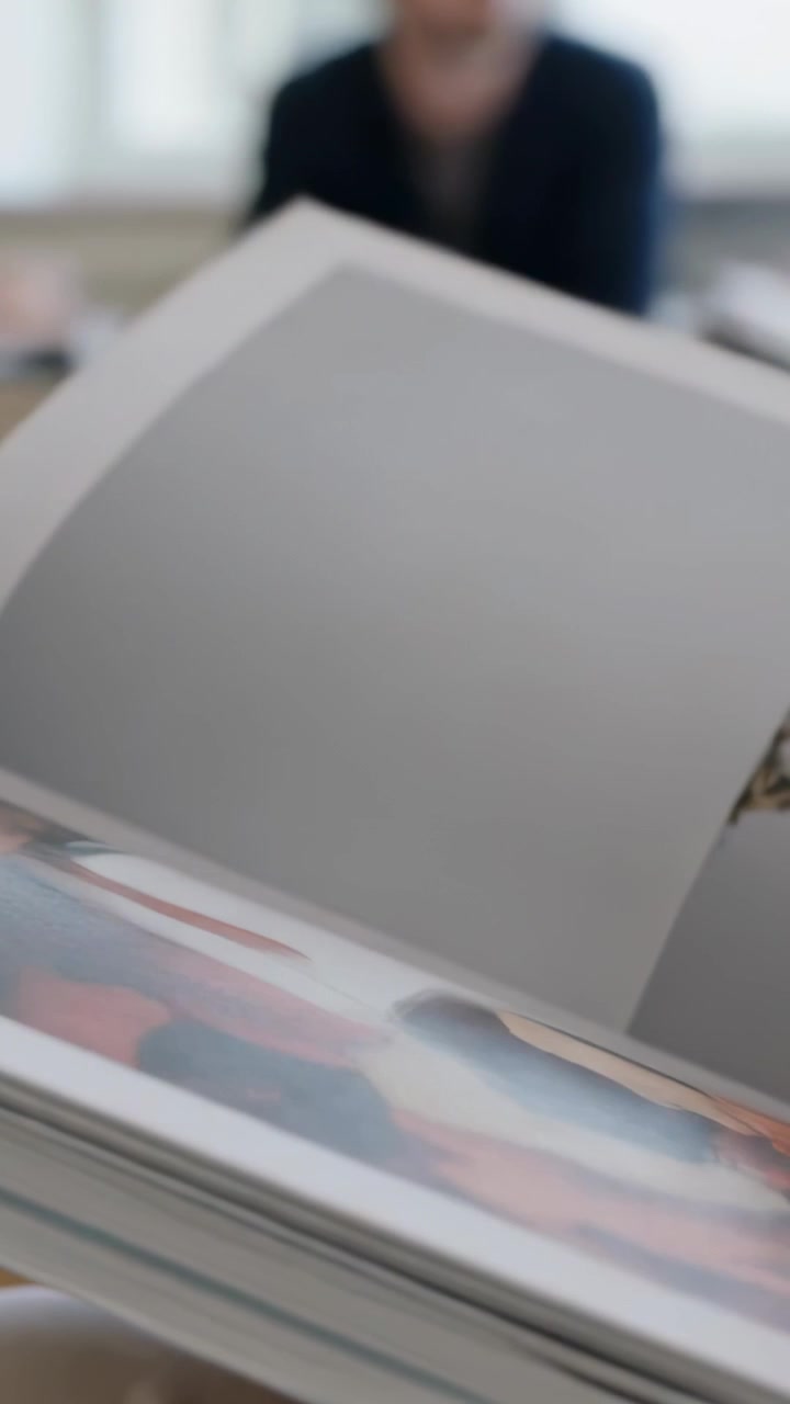 Vertical video: Turning right hand peeling magazine pages at home with observer watching for review
