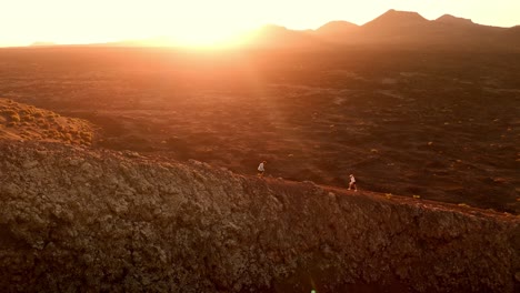 a romantic aerial drone shot of a couple walking together at sunset along the rim of volcano del cuervo in lanzarote, canary islands, spain.