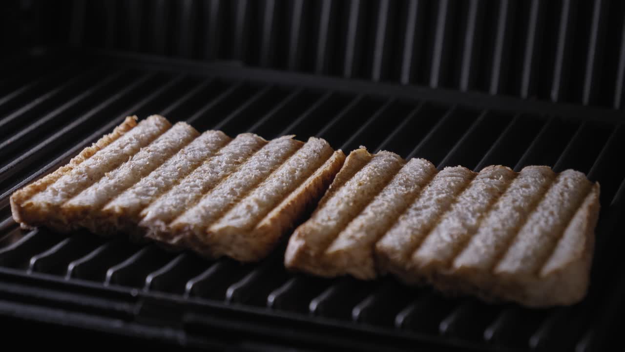 A close up shot of the lid of a sandwich press being opened to reveal two slices of freshly toasted brown bread on a steaming hot grill