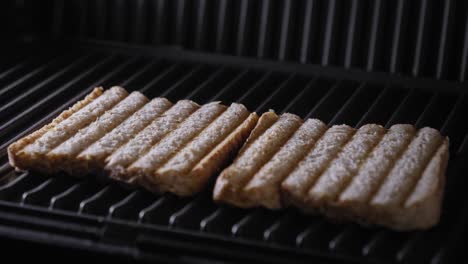 Eine-Nahaufnahme-Des-Deckels-Einer-Sandwichpresse,-Die-Geöffnet-Wird,-Um-Zwei-Scheiben-Frisch-Geröstetes-Schwarzbrot-Auf-Einem-Dampfend-Heißen-Grill-Zu-Enthüllen