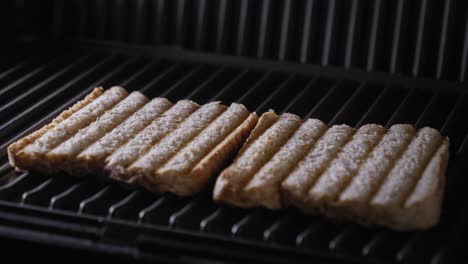 a close up shot of the lid of a sandwich press being opened to reveal two slices of freshly toasted brown bread on a steaming hot grill