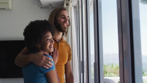 mixed race couple looking out of the window at home