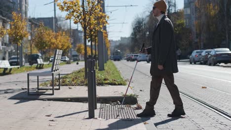 visually impaired man crossing the road with his stick with the help of tactile pedestrian sidewalk for the visually impaired in the city.