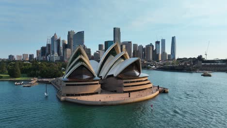 Luftaufnahme-Um-Das-Opernhaus-Von-Sydney-Herum,-Wolkenkratzer-Im-Hintergrund,-Die-Die-Sydney-Harbour-Bridge-Bei-Sonnenuntergang-In-Australien-Freigibt