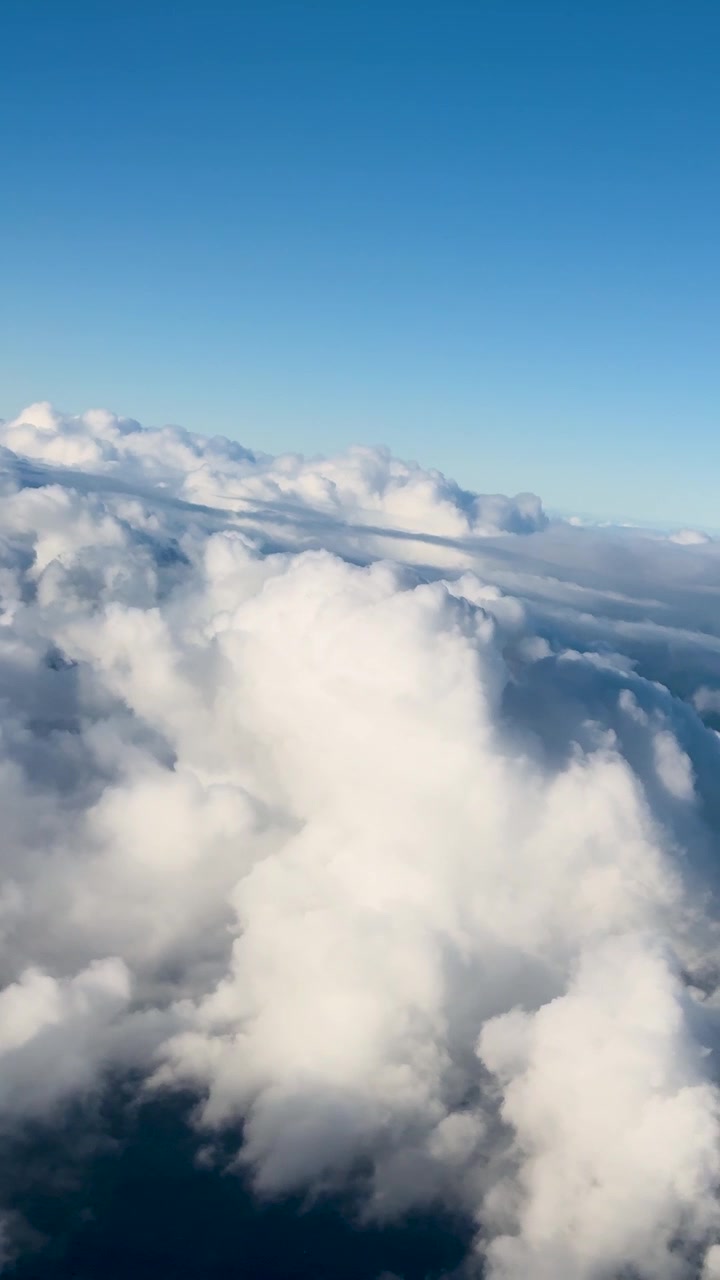 A serene aerial view of fluffy clouds and blue sky, captured from an airplane window, with gentle camera movement