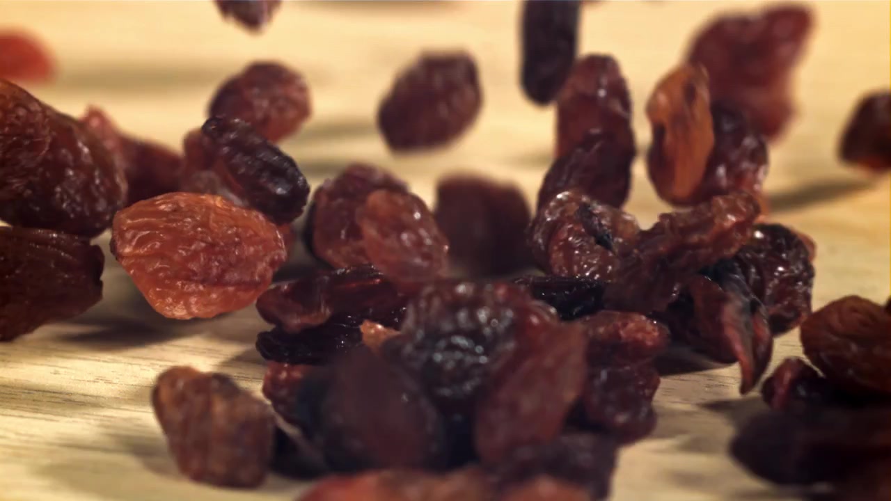 Uvas Passas Caindo em Câmera Lenta sobre uma Superfície de Madeira