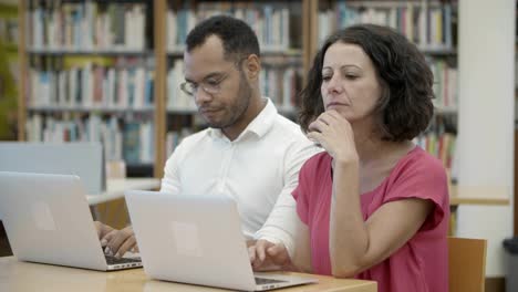 dos personas pensativas que trabajan con una laptop en la biblioteca pública