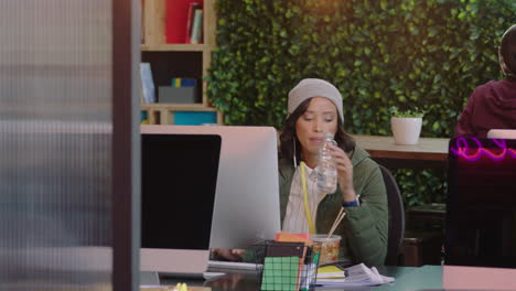 Joven-Mujer-De-Negocios-Afroamericana-Usando-Computadora-Navegando-En-Línea-Escribiendo-Mensajes-De-Correo-Electrónico-Bebiendo-Agua-Escuchando-Música-En-Un-Moderno-Lugar-De-Trabajo-De-Oficina