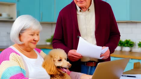 older couple using a laptop, with their small dog beside them.