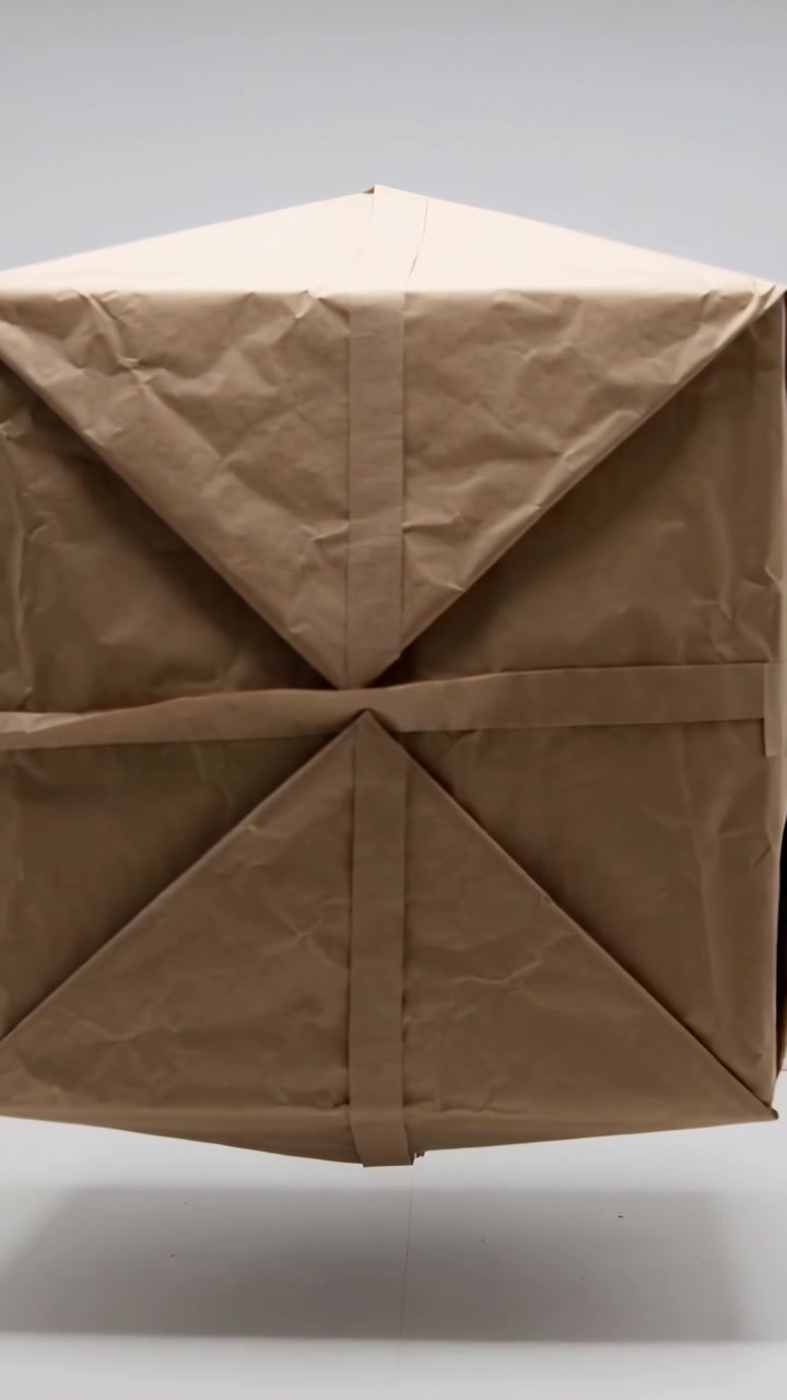 Vertical video: Rotating brown paper cube bobbing in studio on play revealing folds and tape seams