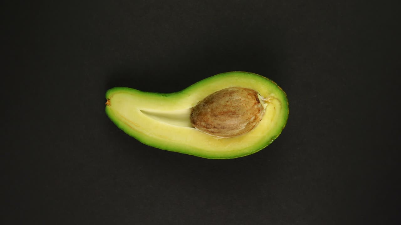 avocado maturo e tagliato in modo biologico ruotando su uno sfondo nero.