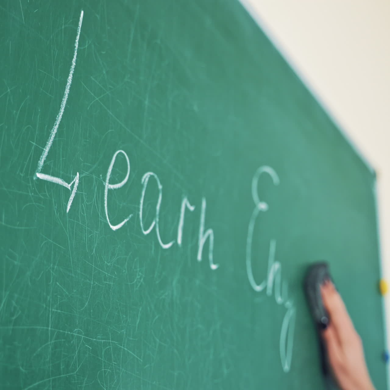 Close-up teacher's hand effaces the chalk from the blackboard. Woman wiping the written English words with a sponge on board in the classroom indoors.