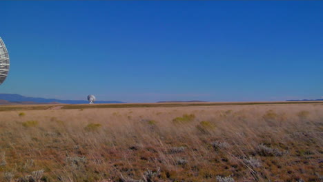 panorámica a través de un campo arrastrado por el viento a una antena parabólica