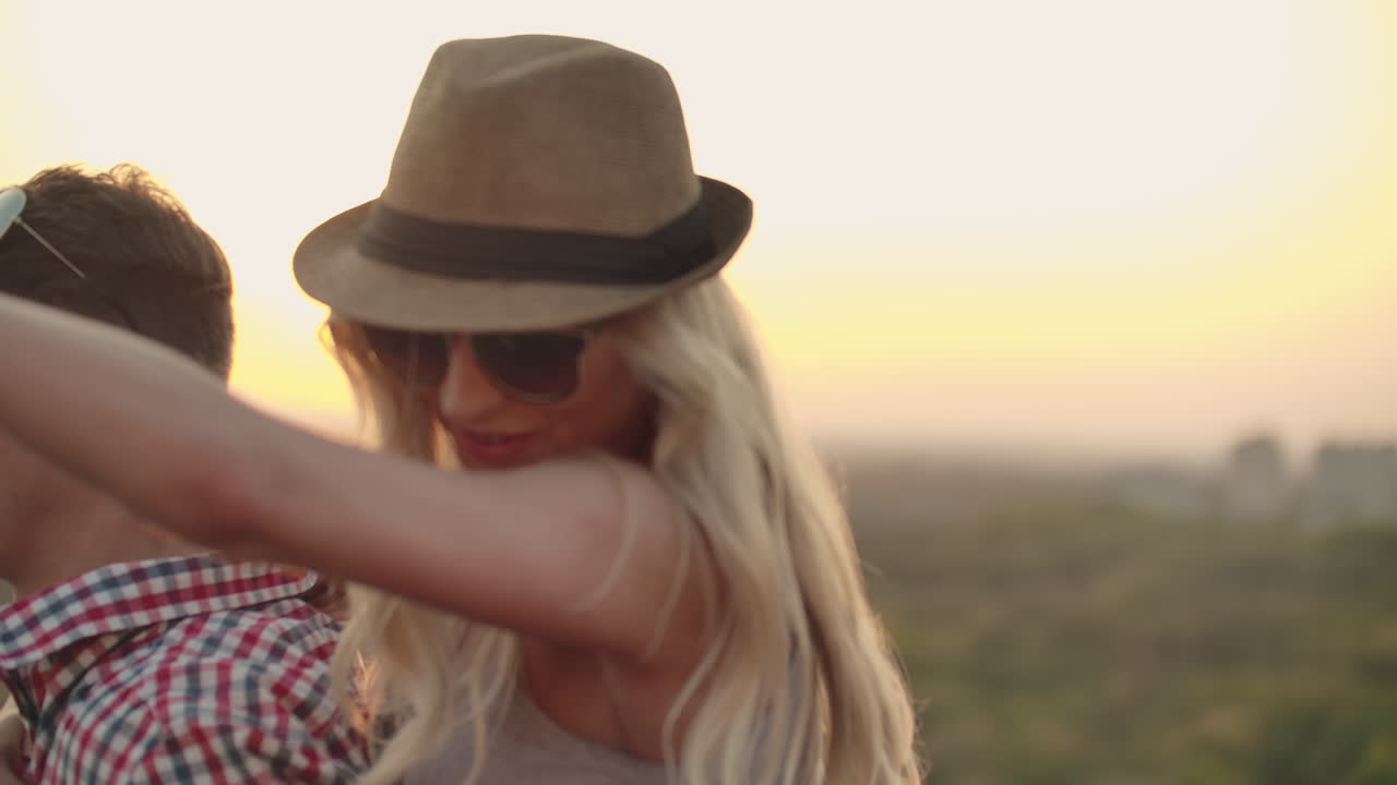 Young couple moves and spins in a dance. Girl with blond hair in a hat and glasses is sitting on her boyfriend's back.