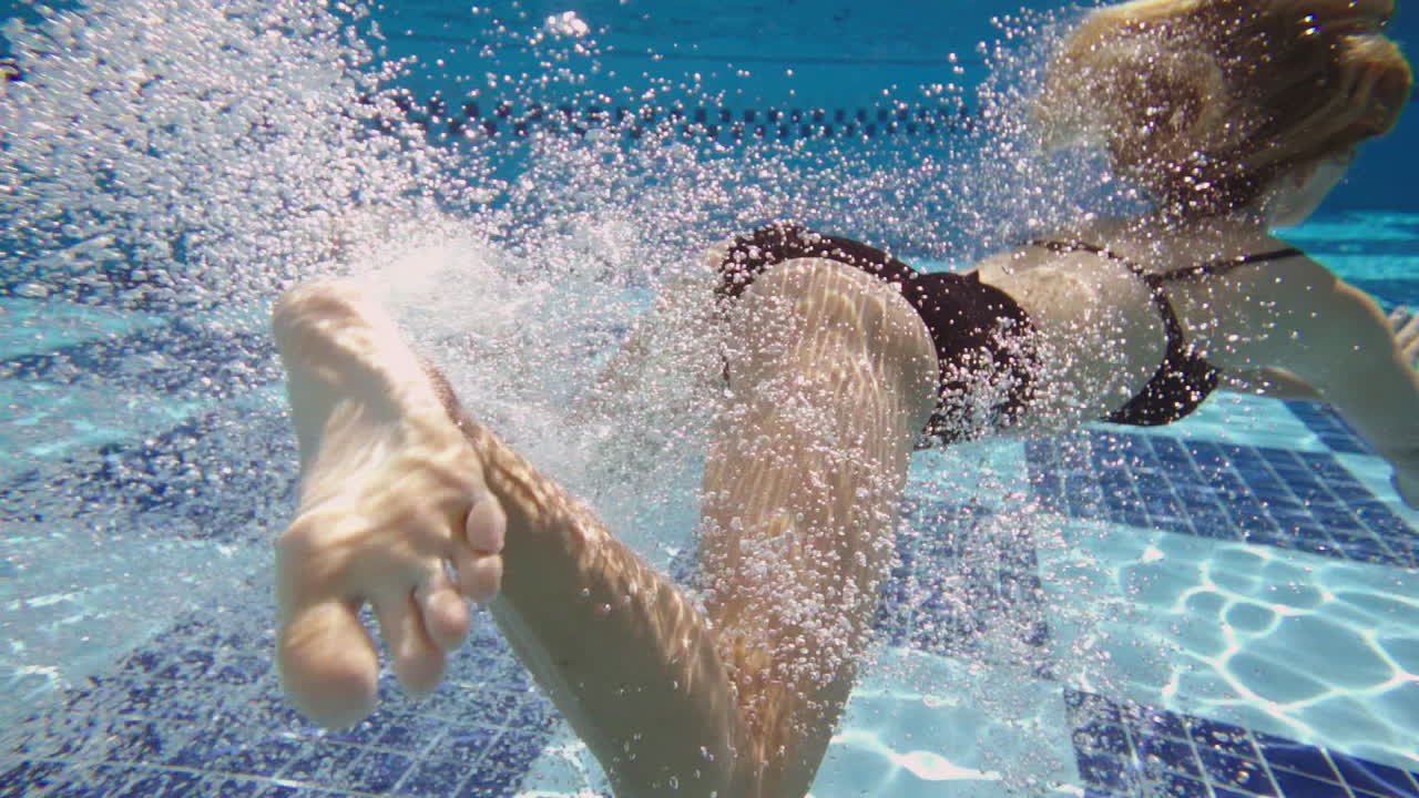 ragazza capelli biondi che salta sott'acqua, riprese dalla piscina