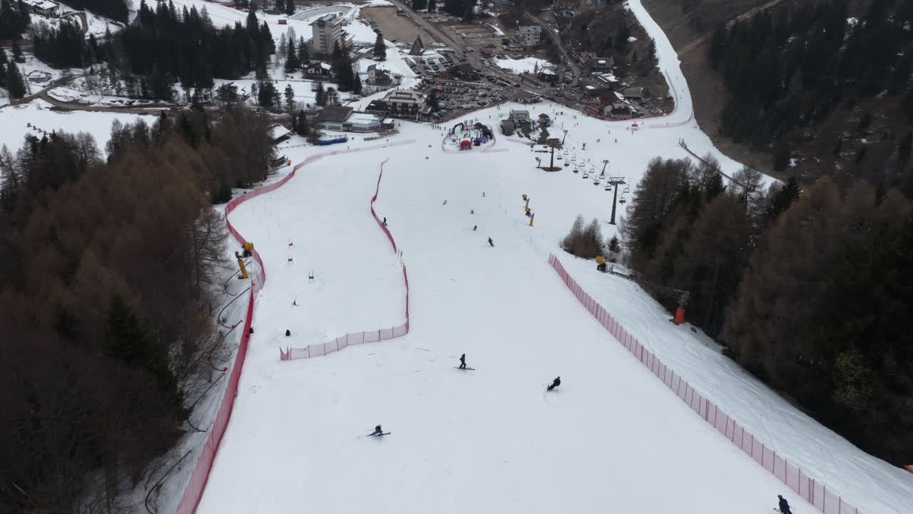 Riprese aeree con drone che catturano un'inquadratura fluida in follow-up di sciatori che scendono una pista a Folgaria, Italia, con una leggera nevicata.