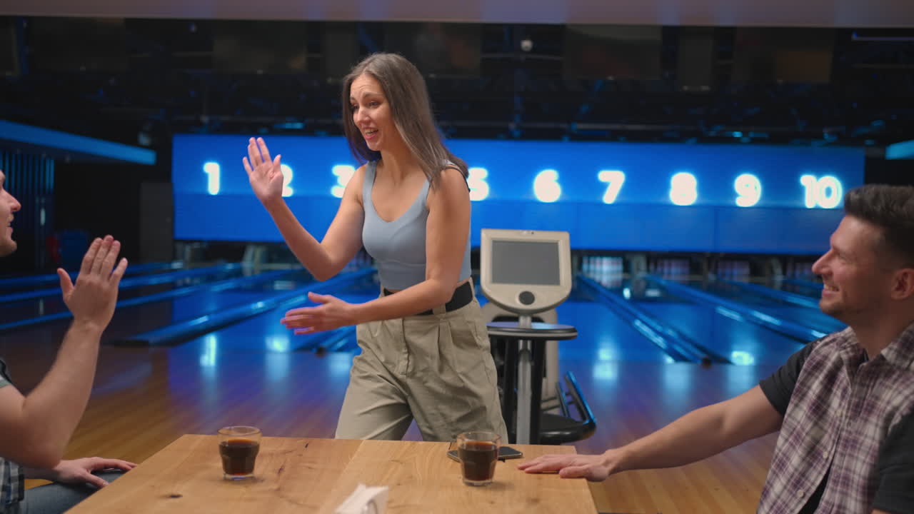Donna felice in una sala da bowling corre gioiosamente dalle sue amiche per festeggiare la serie di strike. Condividi la vittoria con gli amici. Gruppo di amici multietnico.