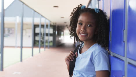 biracial girl with curly hair stands by blue lockers in school, smiling, with copy space