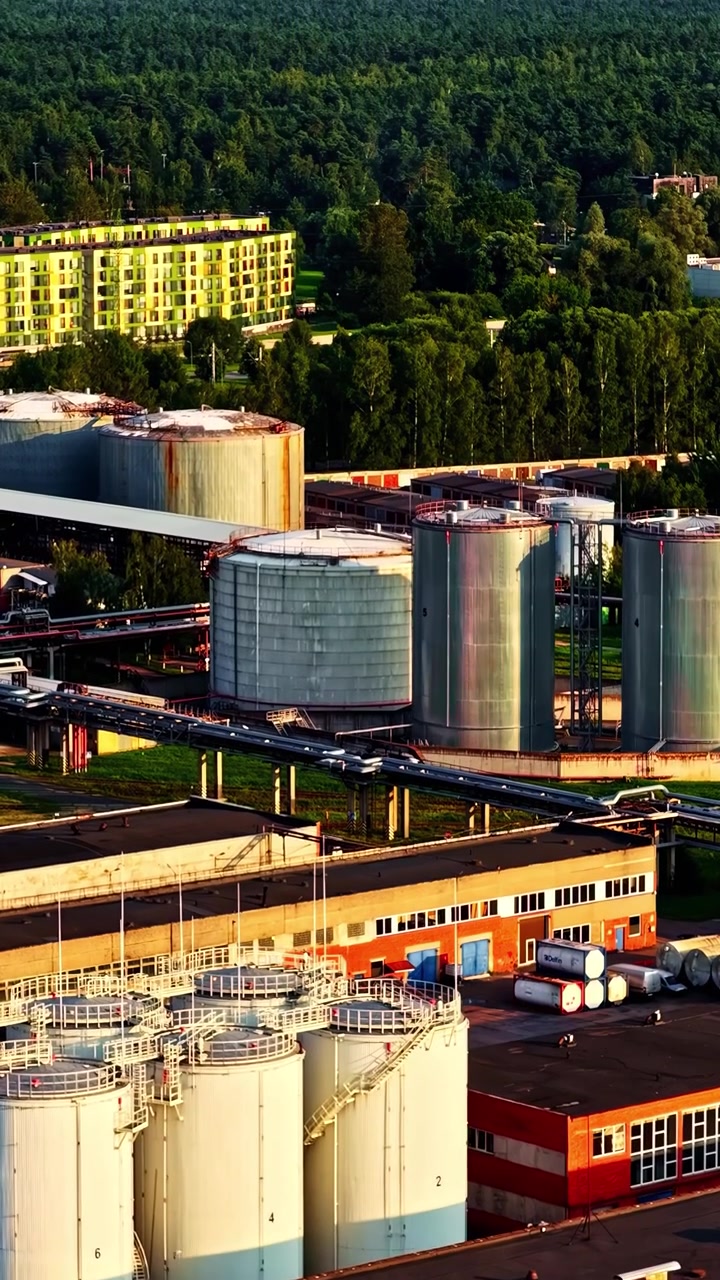 Un sito industriale con grandi serbatoi di stoccaggio ed edifici in mattoni. La calda luce del tramonto proietta lunghe ombre, aggiungendo profondità. Adatto per temi ambientali o industriali.
