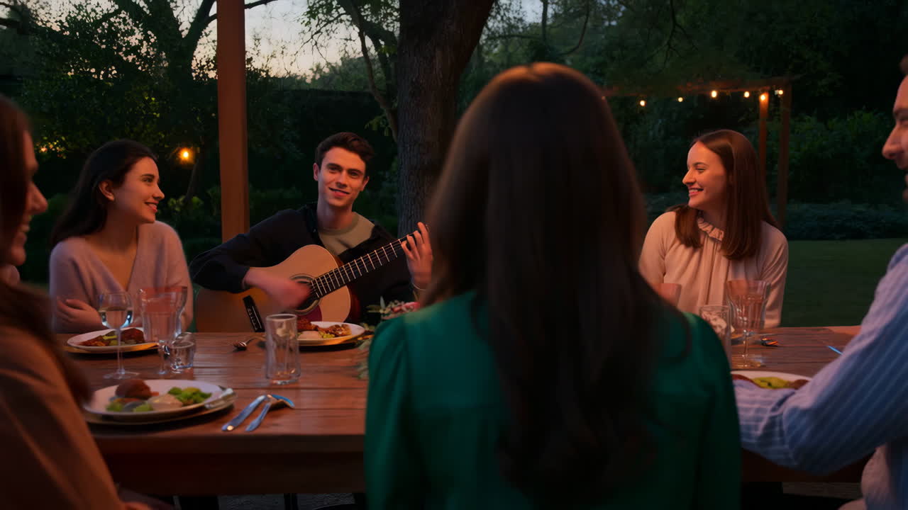Amigos reunidos para una cena al aire libre por la noche con música de guitarra en vivo