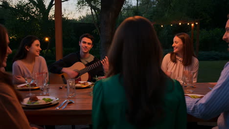 friends gathered for an outdoor evening dinner party with live guitar music