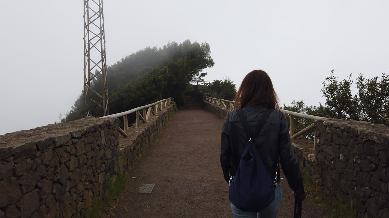 Woman with a backpack walking on a foggy mountain bridge in Tenerife, Canary Islands