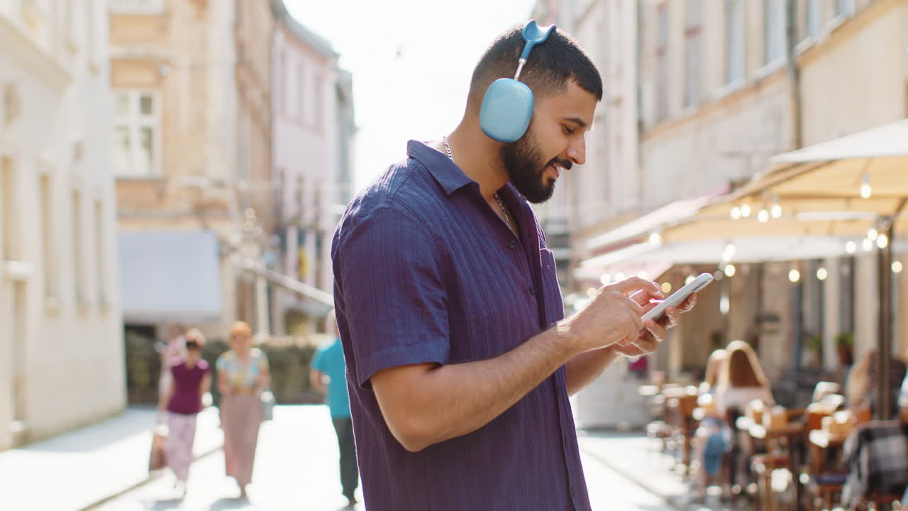 Happy young man in wireless headphones choosing listening music in smartphone dancing outdoors