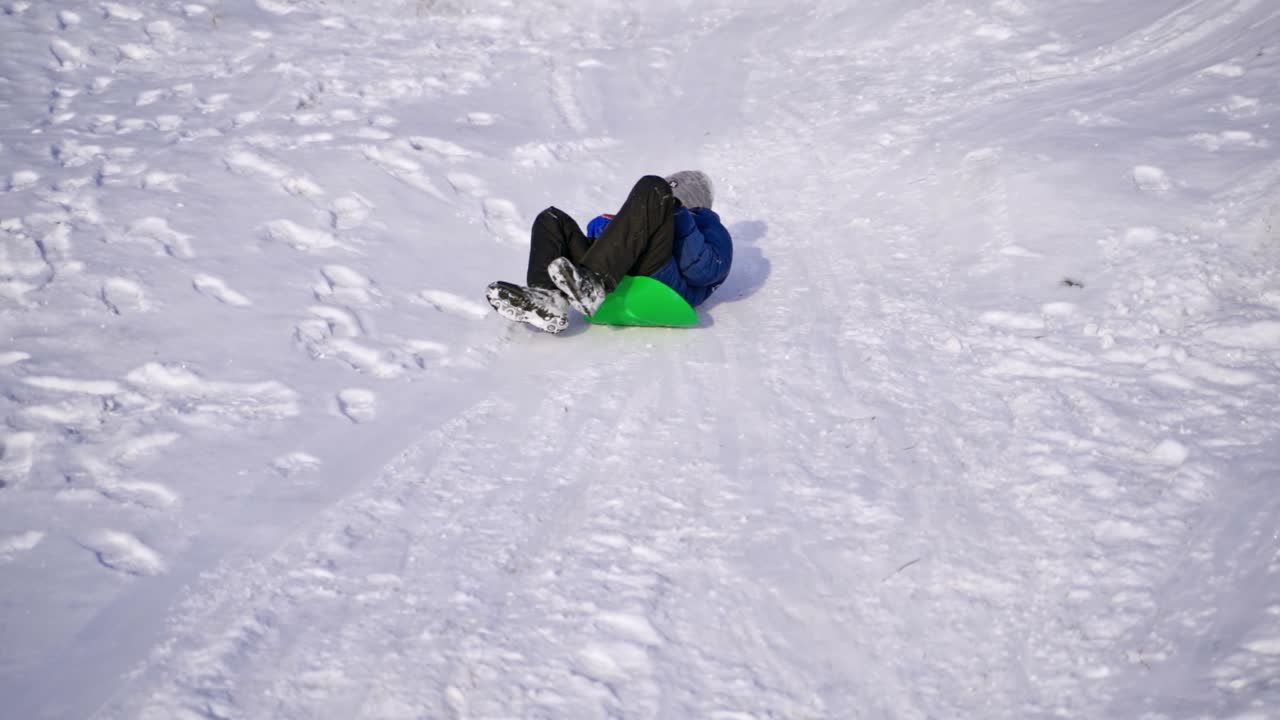 View from below on a boy sledding. Cute child riding from snow slide in winter. Cheerful vacation. Slow motion.
