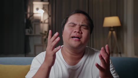 frustrated disappointed asian fat man watches tv while sitting on a couch at home in the evening