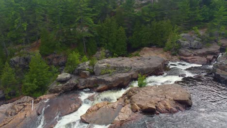 water shimmers flowing and cascading across smooth rocks down waterfall river in forest, aerial tracking